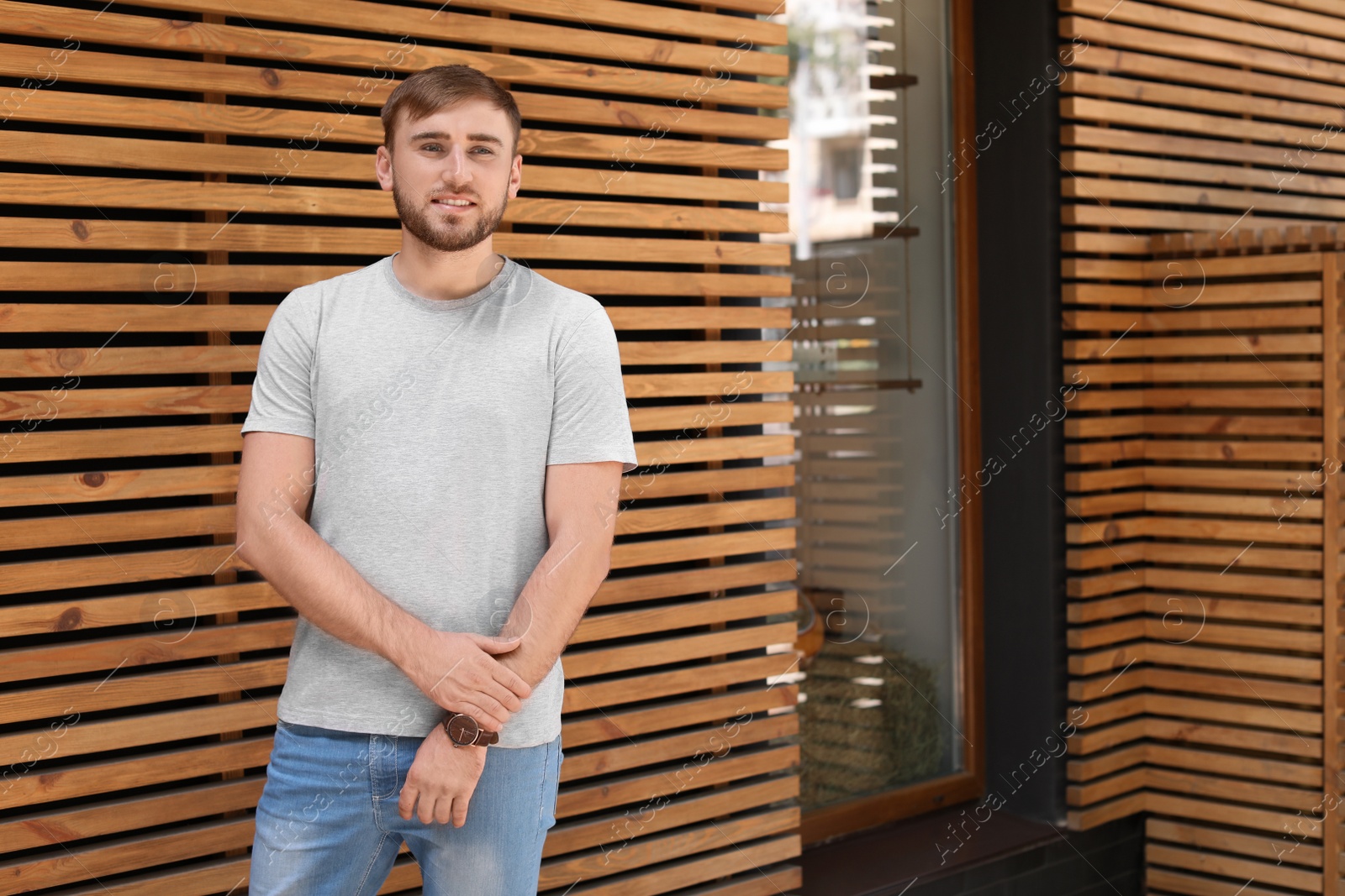 Photo of Young man wearing gray t-shirt near wooden wall on street. Urban style