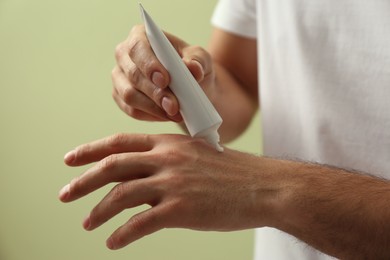 Man applying cream from tube onto hand on green background, closeup