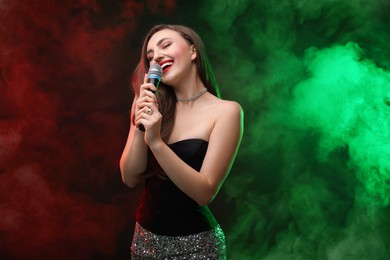 Beautiful woman with microphone singing on stage in color lighted smoke
