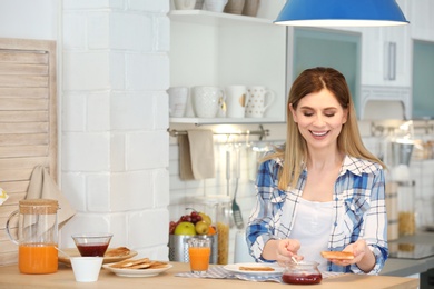 Photo of Beautiful woman spreading jam on toasted bread at table