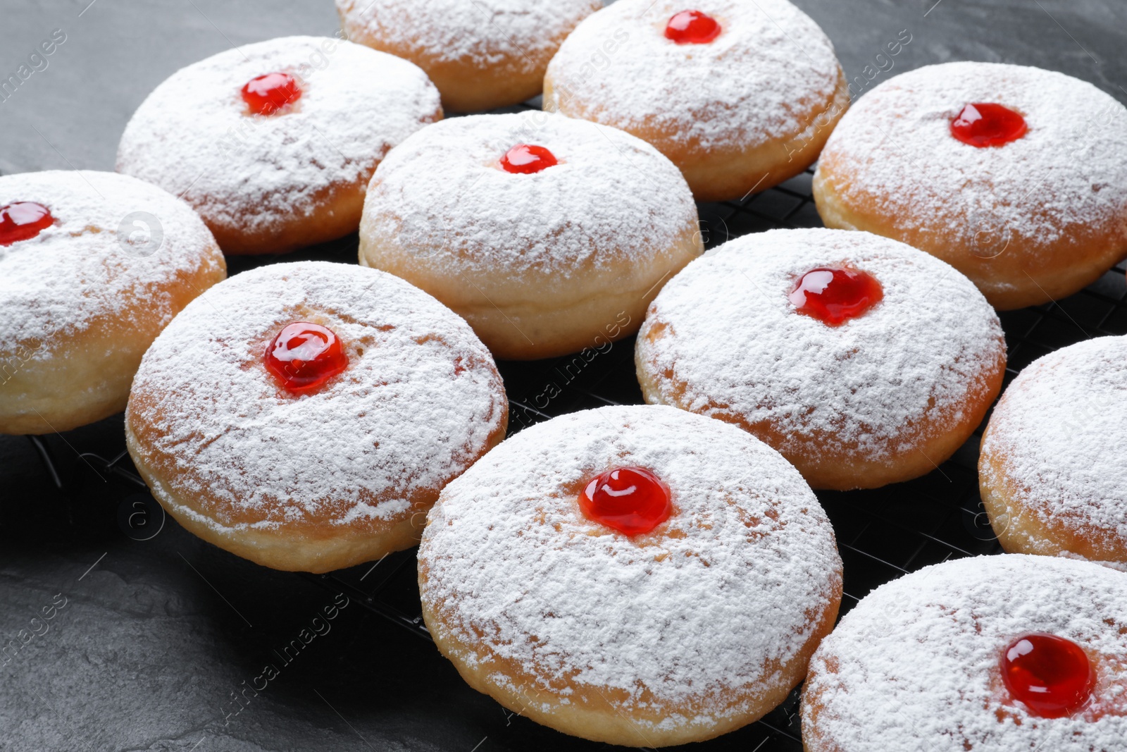 Photo of Many delicious donuts with jelly and powdered sugar on black table