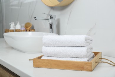 Photo of Wooden tray with rolled bath towels on white table in bathroom