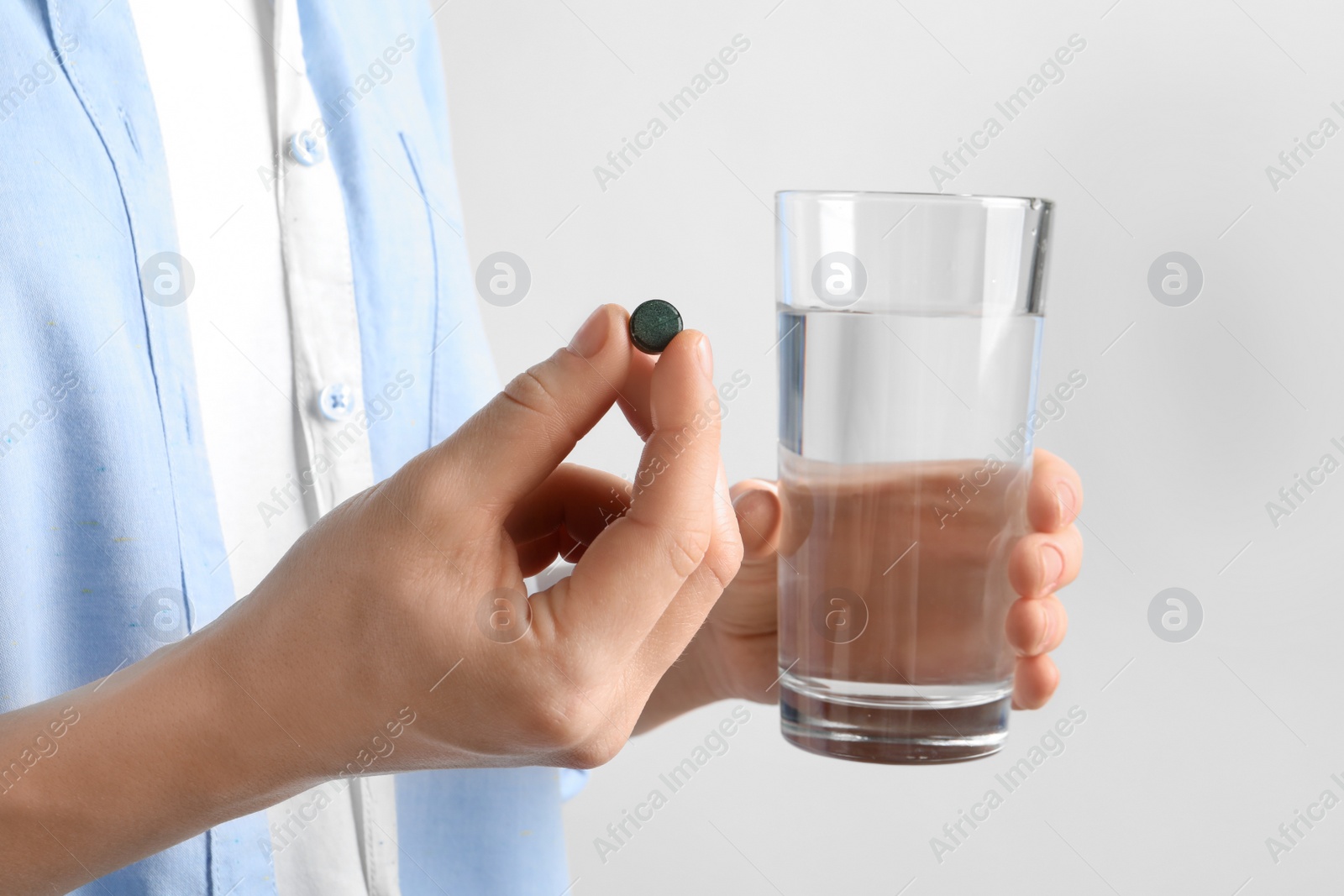 Photo of Woman holding spirulina pill and glass of water, closeup