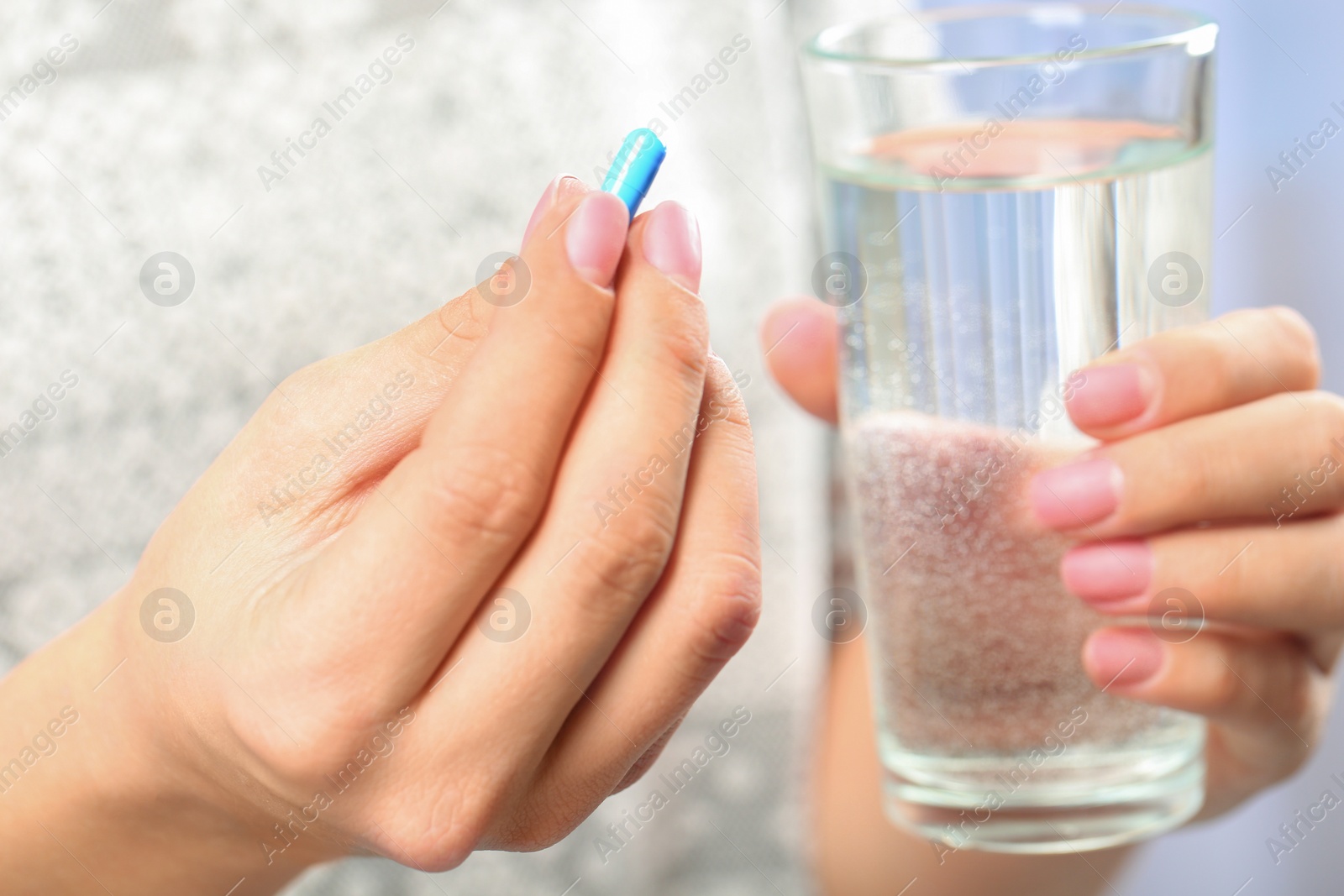 Photo of Woman holding pill and glass of water on blurred background, closeup. Space for text