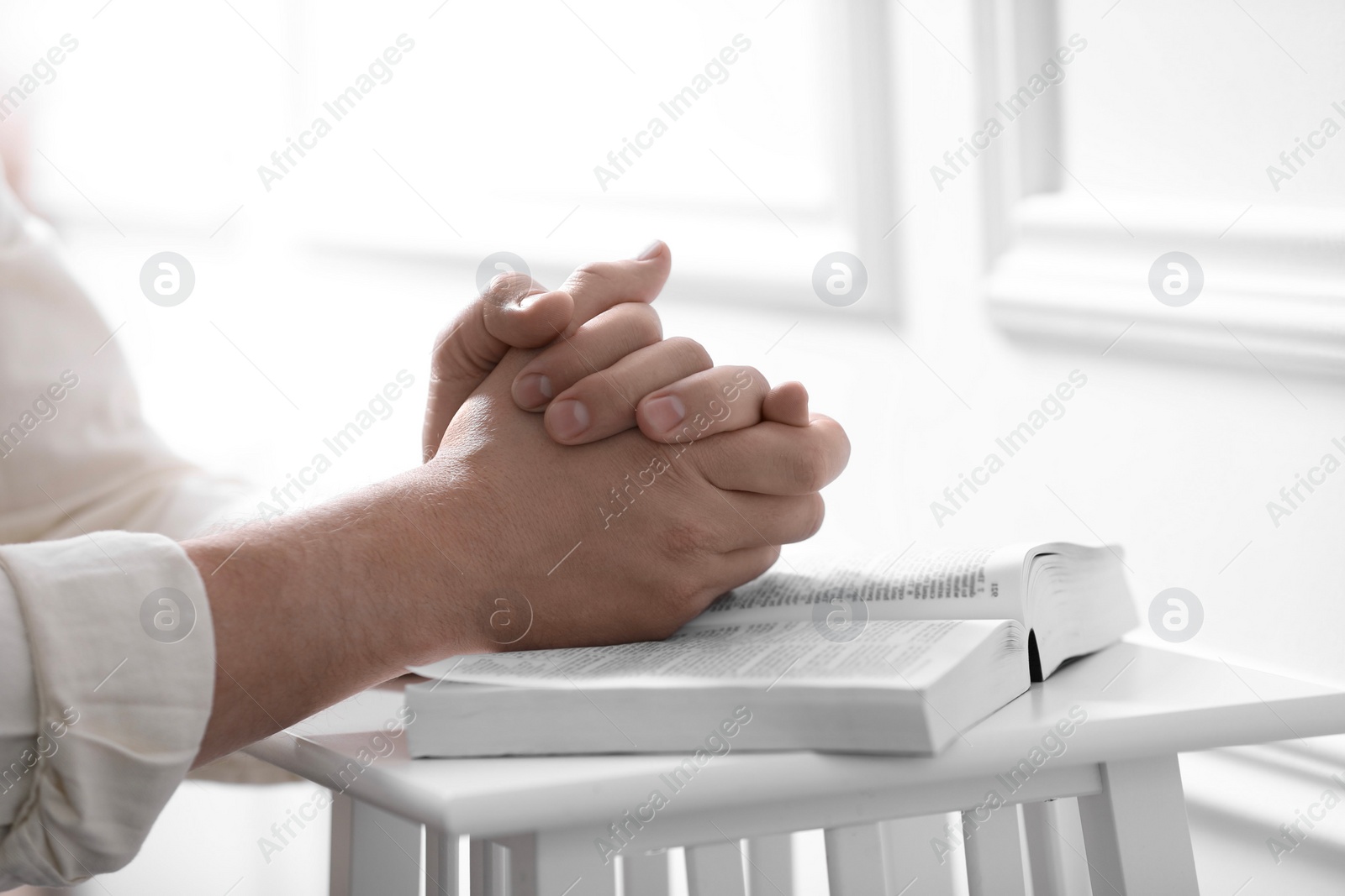 Photo of Religion. Christian man praying over Bible indoors, closeup