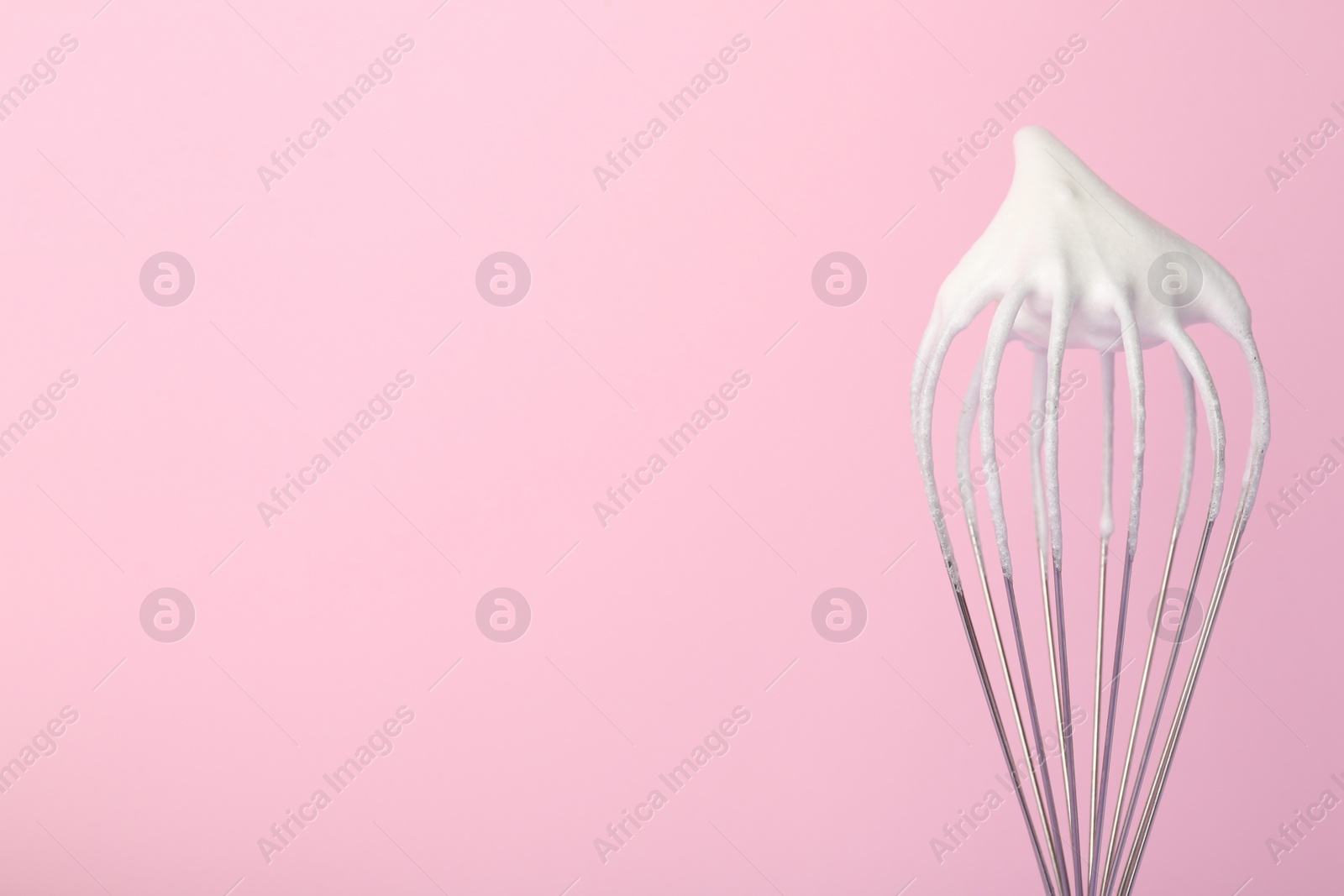 Photo of Whisk with whipped egg whites on pink background, closeup. Space for text