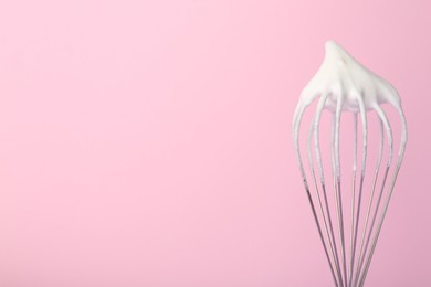 Whisk with whipped egg whites on pink background, closeup. Space for text