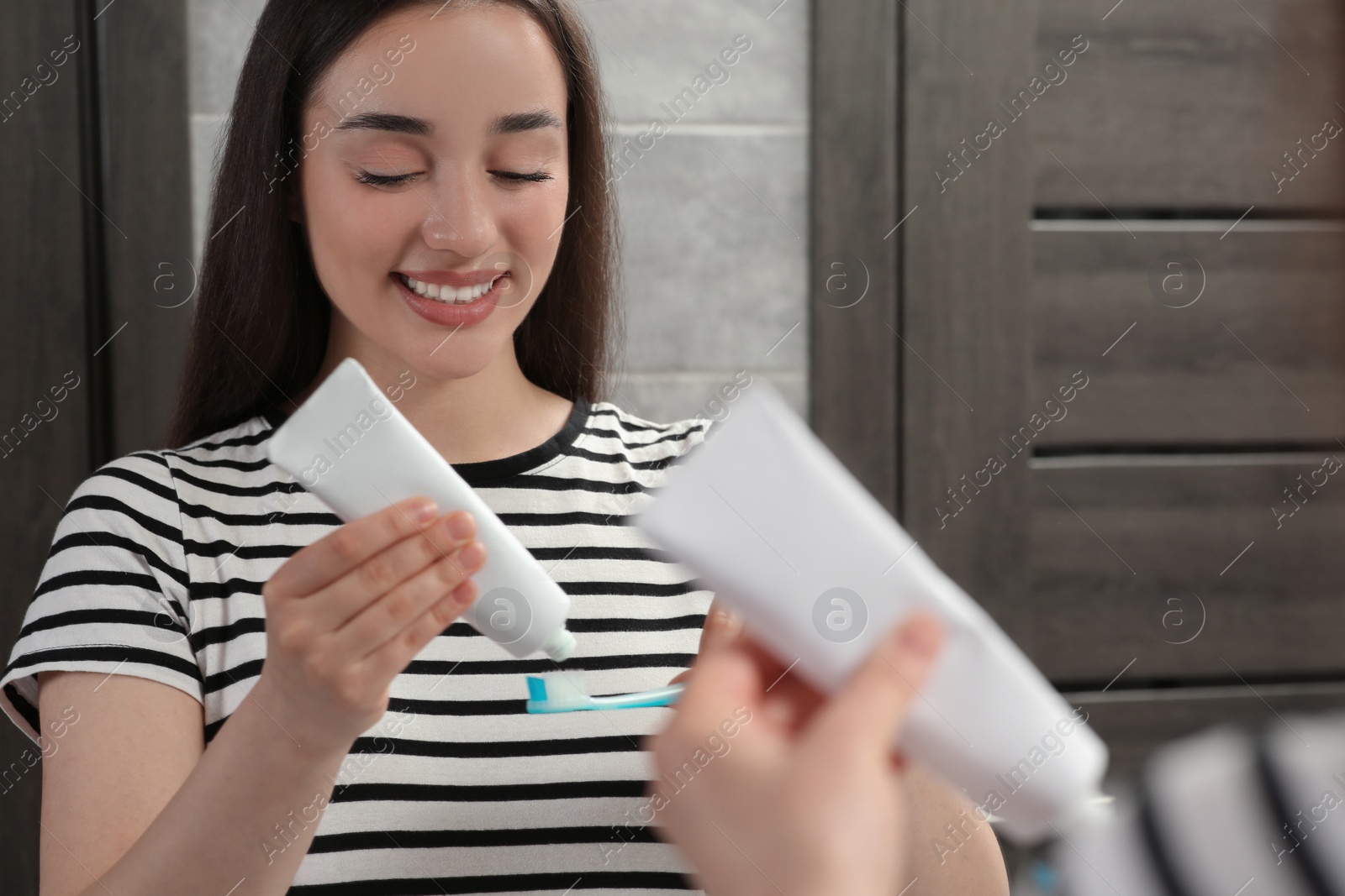 Photo of Young woman squeezing toothpaste from tube onto toothbrush near mirror in bathroom