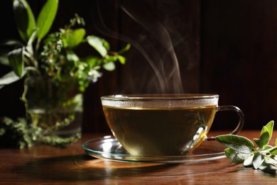 Photo of Cup of aromatic herbal tea and sage on wooden table