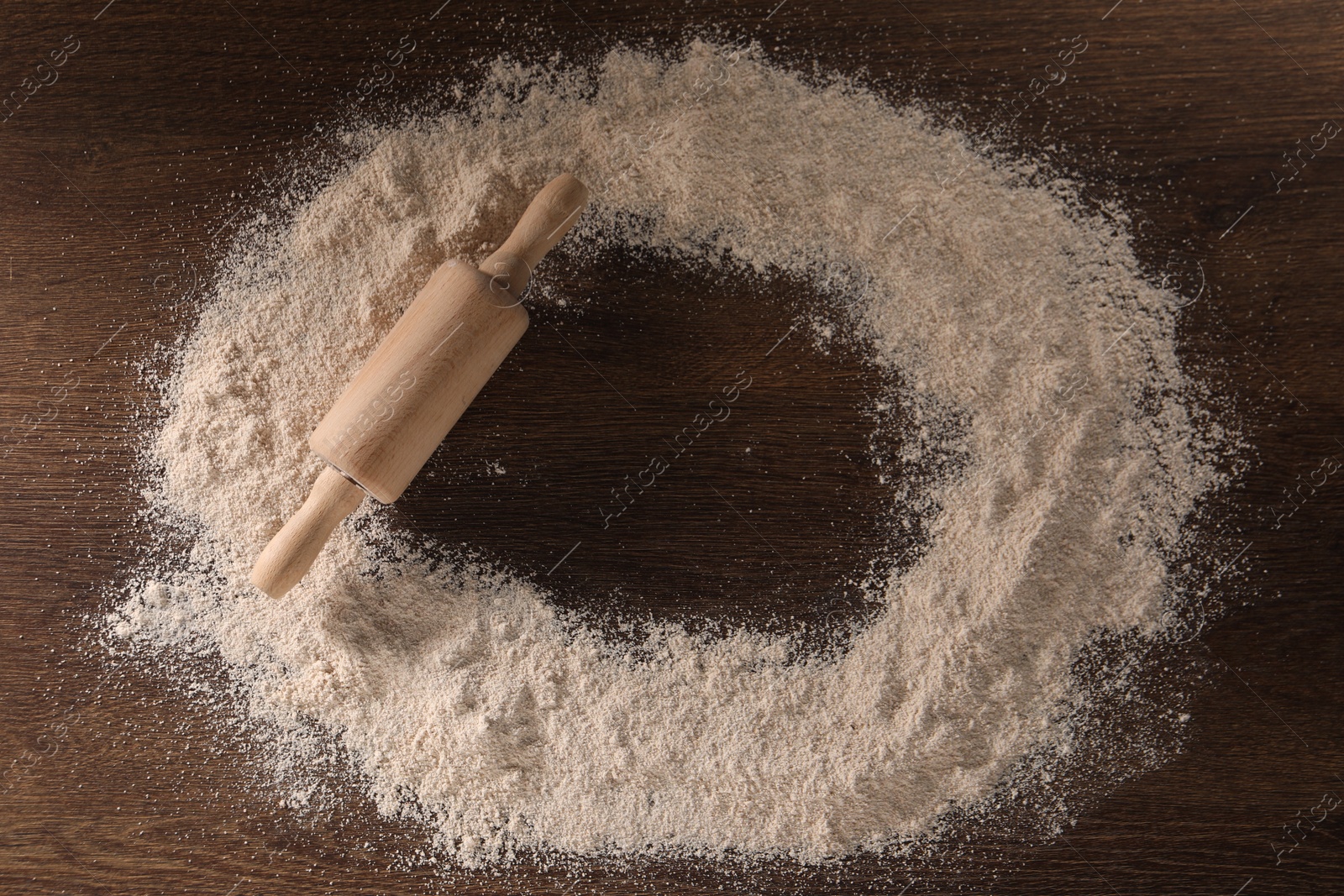 Photo of Frame of flour and rolling pin on wooden table, top view. Space for text