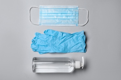 Photo of Medical gloves, mask and hand sanitizer on grey background, flat lay
