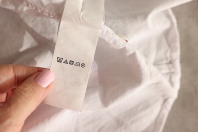 Photo of Woman holding clothing label in different languages on white garment, closeup