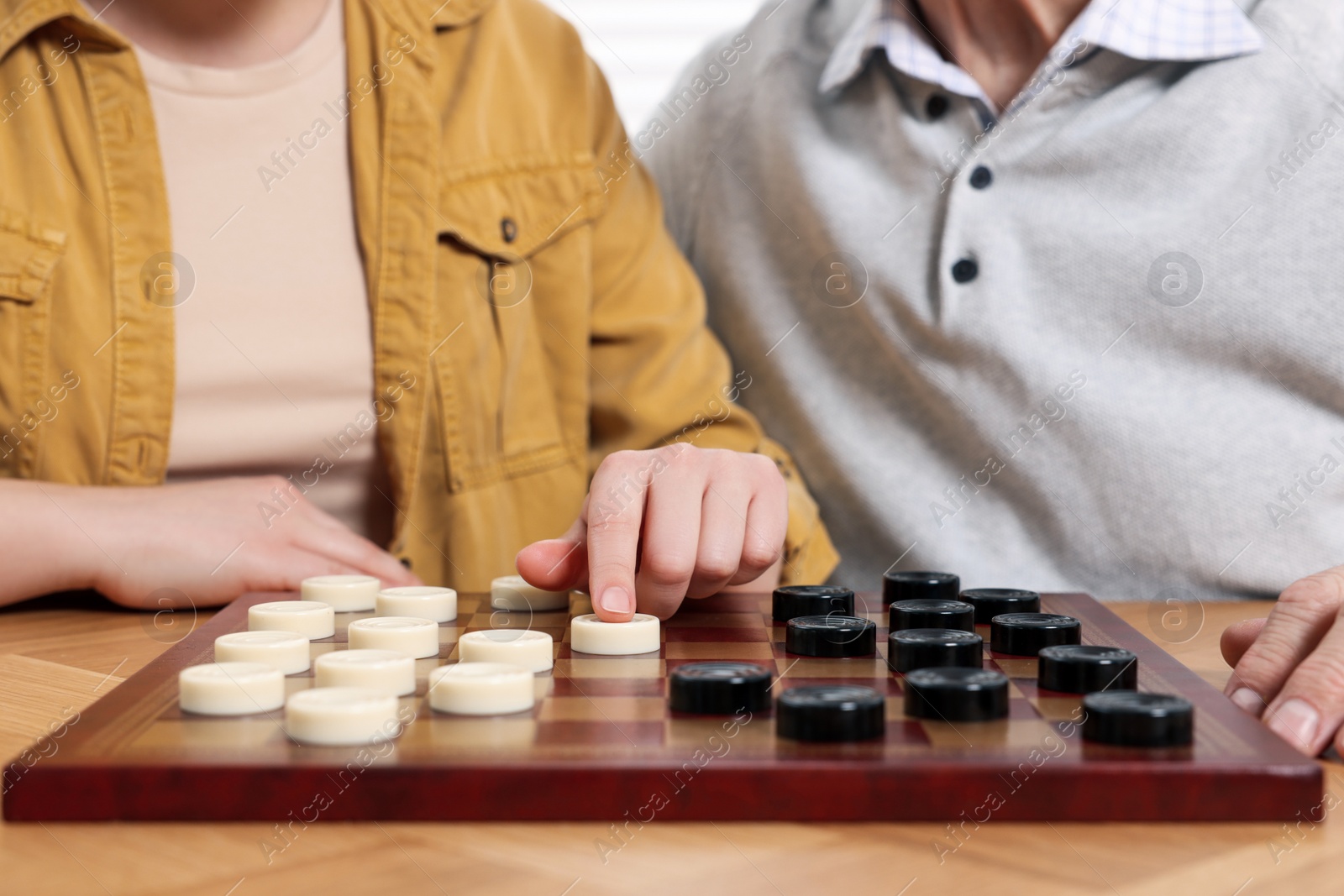 Photo of Playing checkers. Senior man learning woman at table in room, closeup