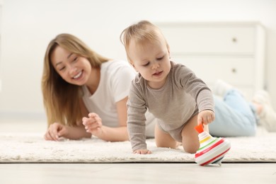 Children toys. Happy mother and her little son playing with spinning top on rug at home, selective focus