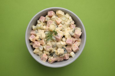 Photo of Tasty Olivier salad with boiled sausage in bowl on green table, top view