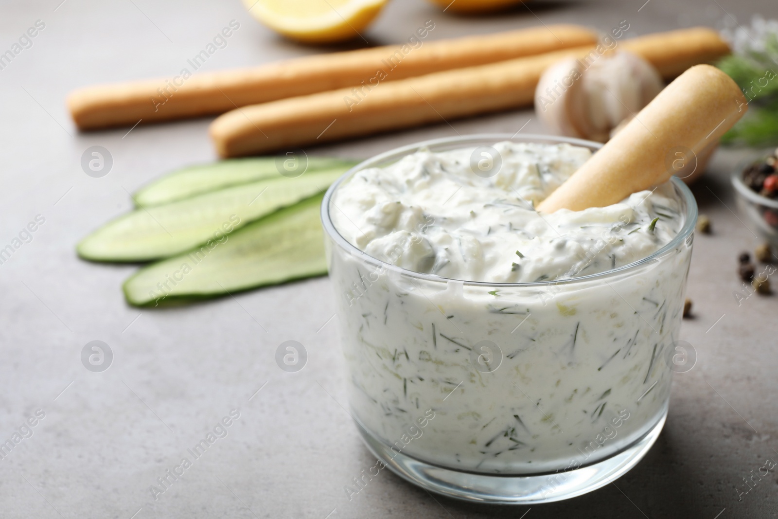 Photo of Bread stick in bowl of cucumber sauce with ingredients on grey background, space for text. Traditional Tzatziki