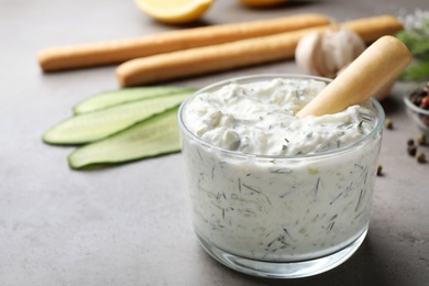 Photo of Bread stick in bowl of cucumber sauce with ingredients on grey background, space for text. Traditional Tzatziki