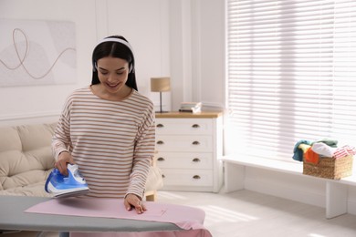 Photo of Young woman listening to music while ironing clothes at home. Space for text
