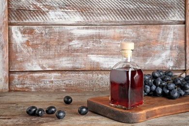 Photo of Glass bottle with wine vinegar and fresh grapes on wooden table. Space for text