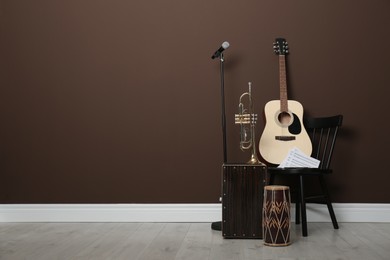 Photo of Acoustic guitar, trumpet, hand drum and microphone near brown wall indoors, space for text. Musical instruments