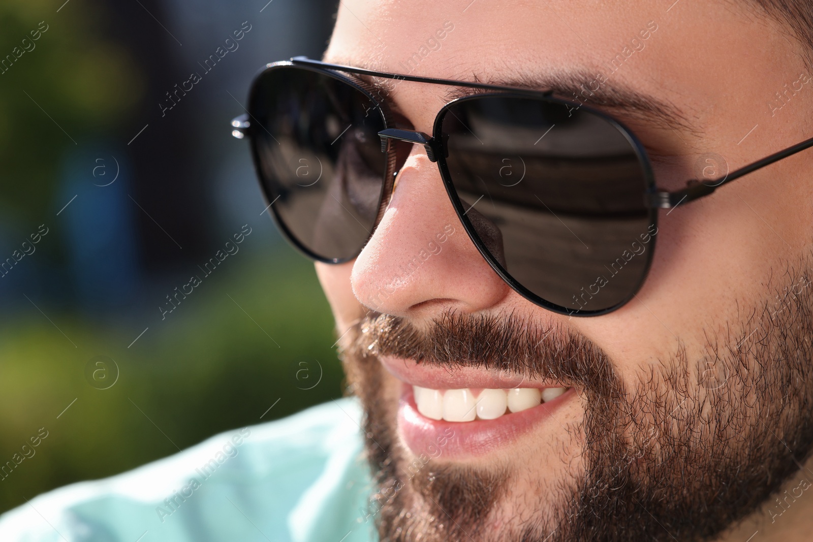 Photo of Handsome smiling man in sunglasses outdoors, closeup. Space for text