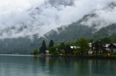 Blurred view of beautiful village on lake shore near mountains