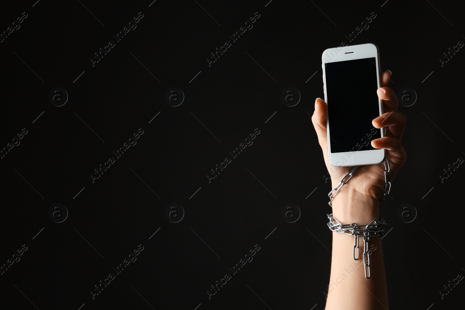 Photo of Woman chained to smartphone on black background, closeup with space for text. Loneliness concept