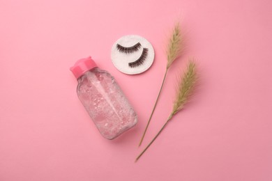 Bottle of makeup remover, cotton pad, spikelets and false eyelashes on pink background, flat lay