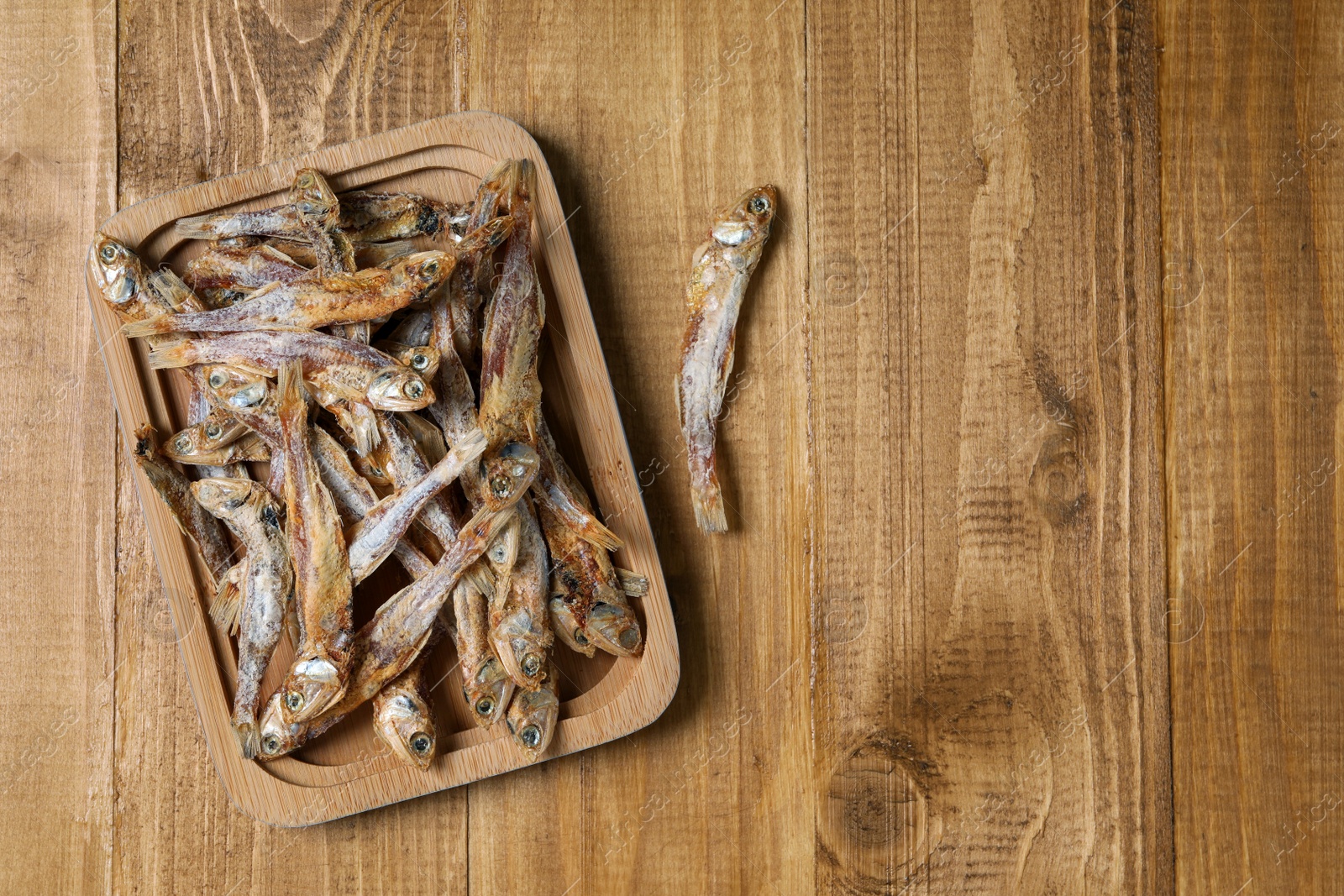 Photo of Plate of tasty dried anchovies on wooden table, flat lay. Space for text