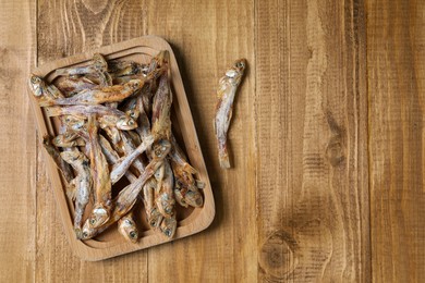 Photo of Plate of tasty dried anchovies on wooden table, flat lay. Space for text