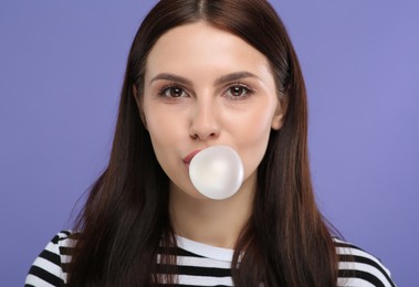 Beautiful woman blowing bubble gum on light purple background