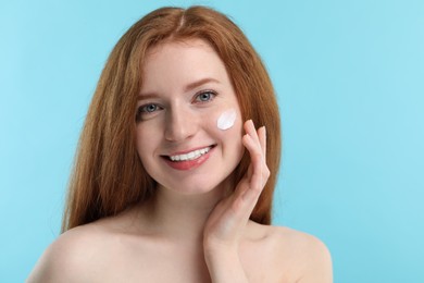 Photo of Smiling woman with freckles and cream on her face against light blue background