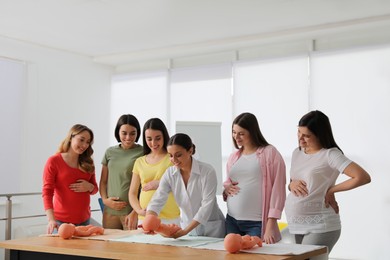 Photo of Pregnant women learning how to swaddle baby at courses for expectant mothers indoors