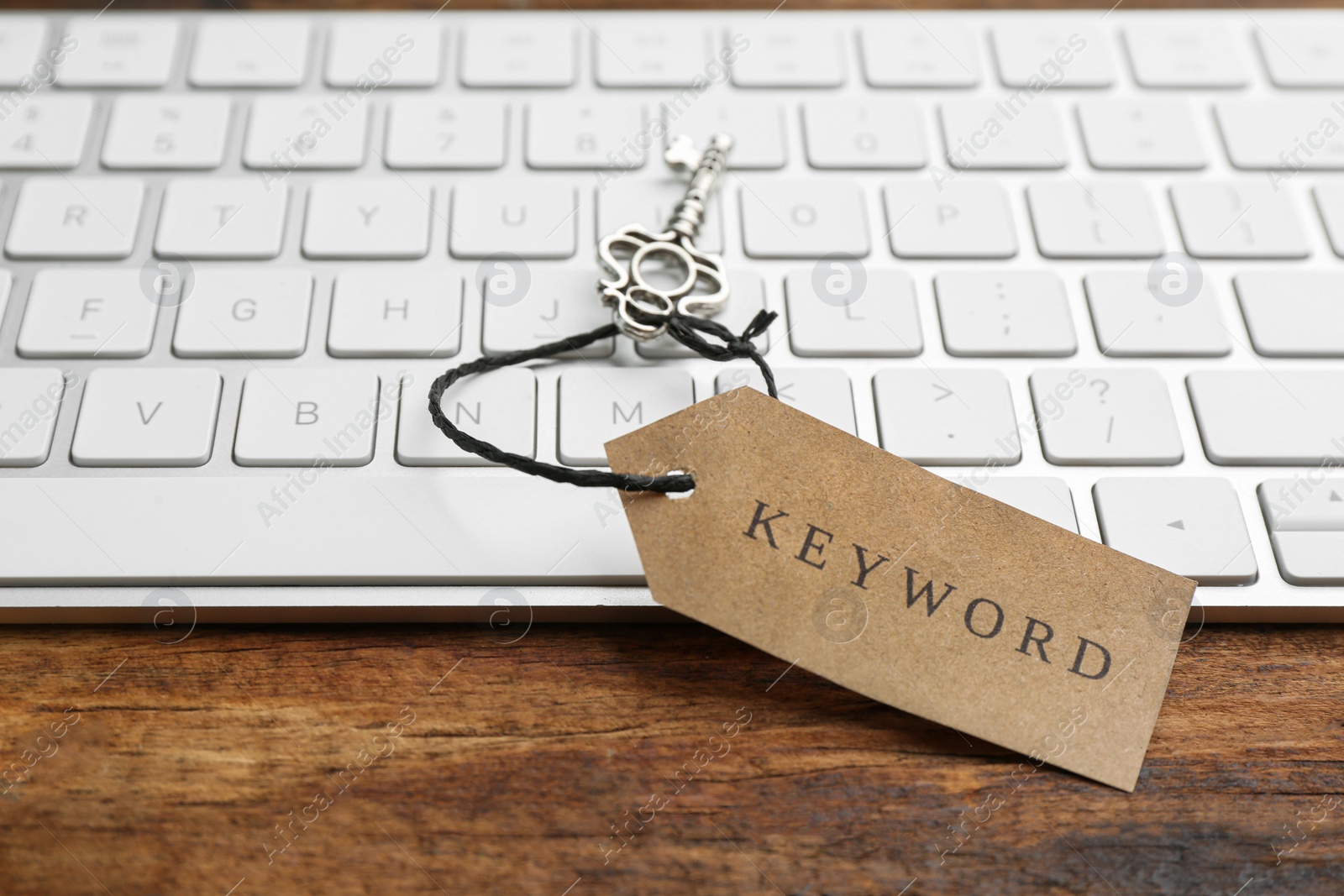 Photo of Keyboard, vintage key and tag with word KEYWORD on wooden table, closeup