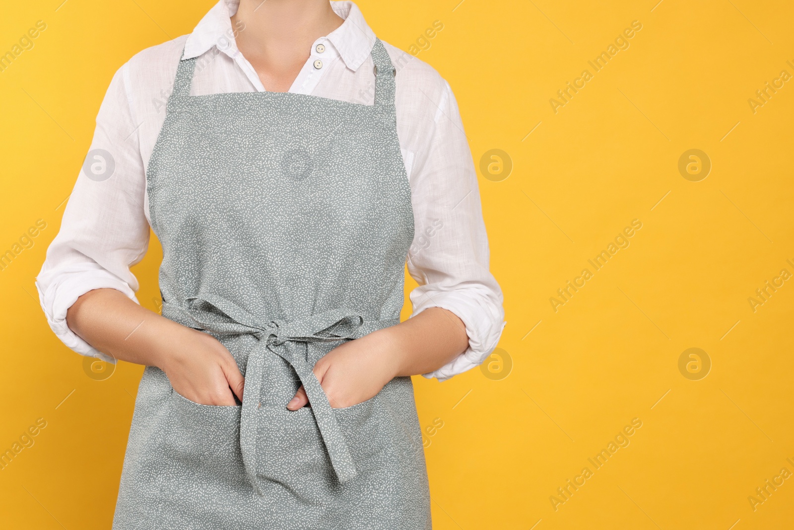 Photo of Woman in clean apron with pattern on orange background, closeup. Space for text