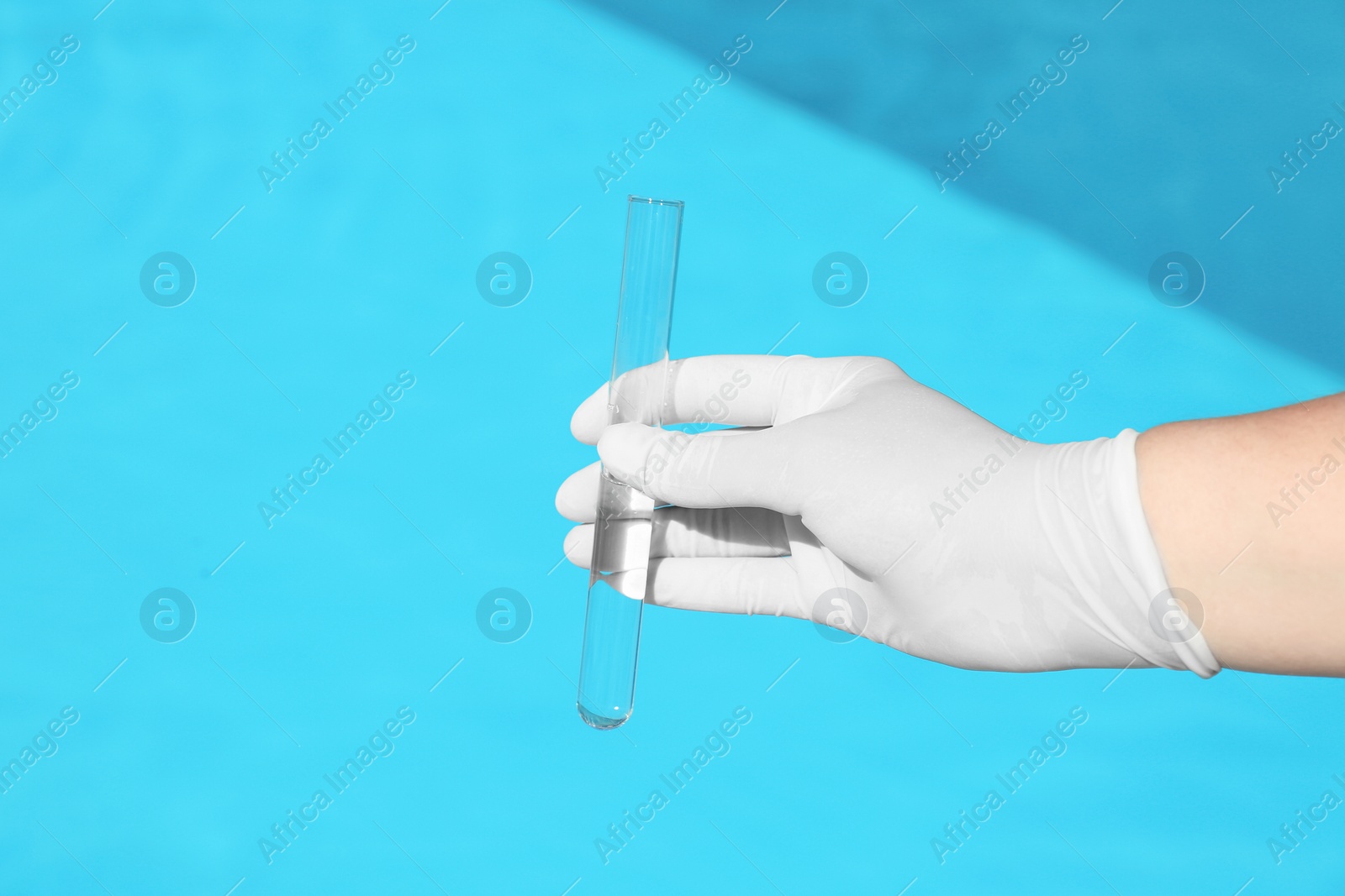 Photo of Woman holding glass tube with sample of swimming pool water to check PH level outdoors, closeup