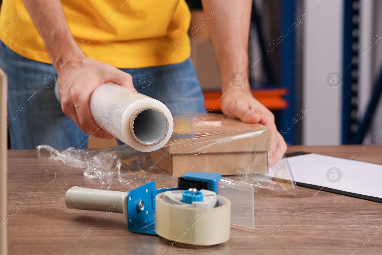 Photo of Post office worker wrapping parcel in stretch film at counter indoors, closeup