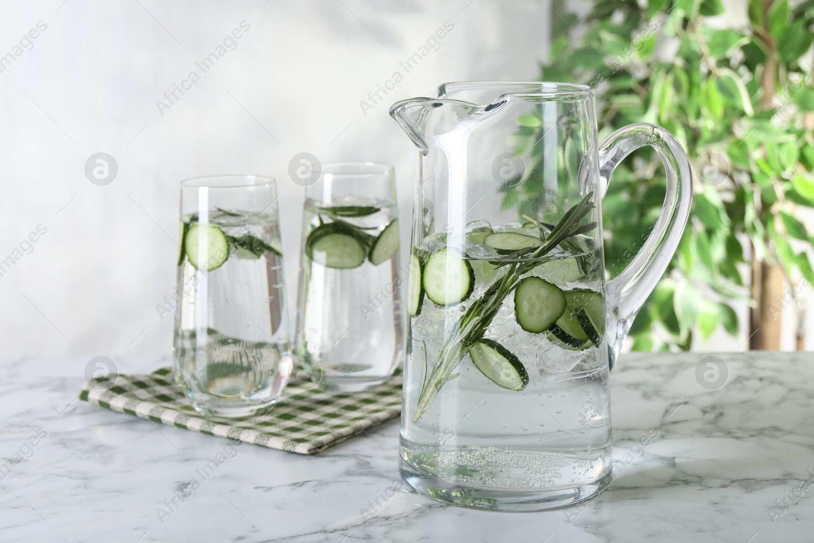 Photo of Refreshing cucumber water with rosemary in jug on white marble table