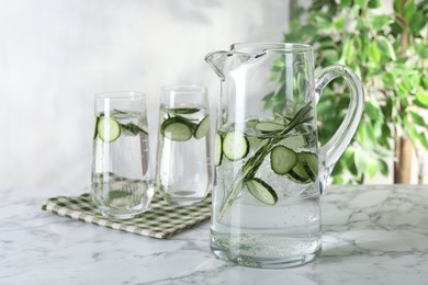 Photo of Refreshing cucumber water with rosemary in jug on white marble table