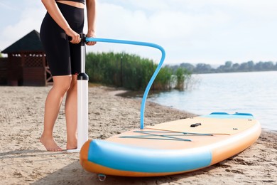 Photo of Woman pumping up SUP board on river shore, closeup