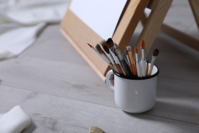 Photo of Different brushes near stand with canvas on floor in artist's studio, space for text