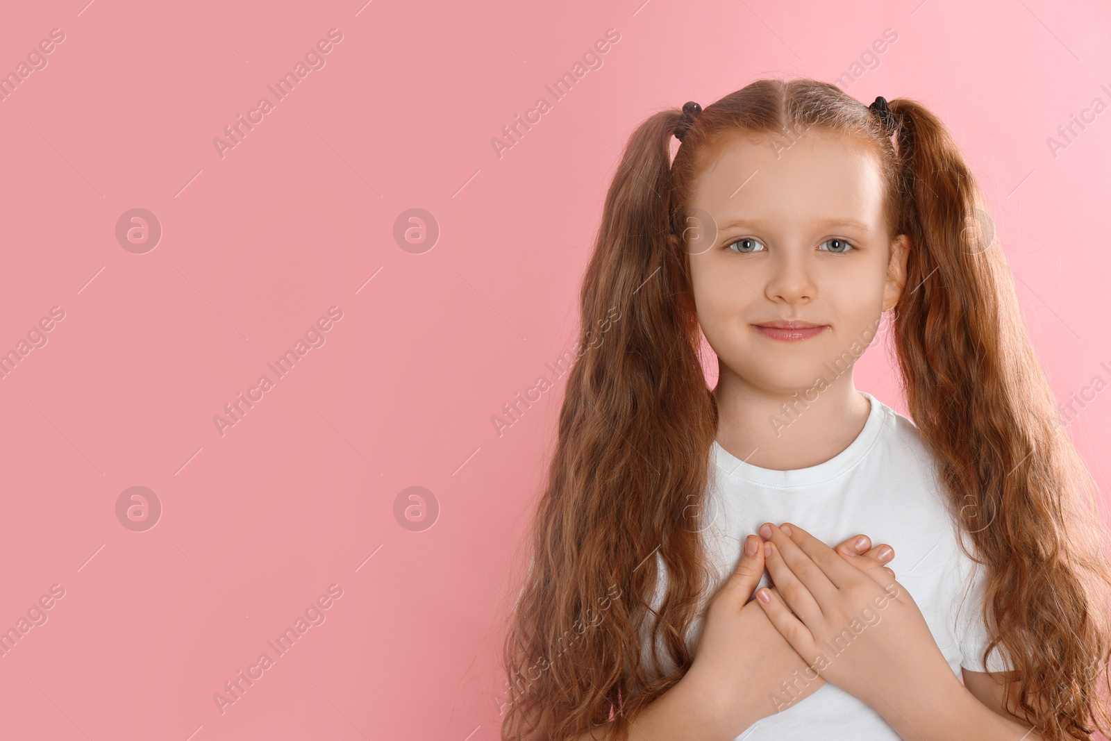 Photo of Cute grateful little girl with hands on chest against pink background. Space for text