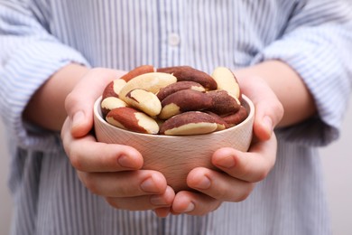 Photo of Woman holding bowl with tasty Brazil nuts, closeup