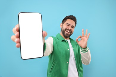 Photo of Young man showing smartphone in hand and OK gesture on light blue background