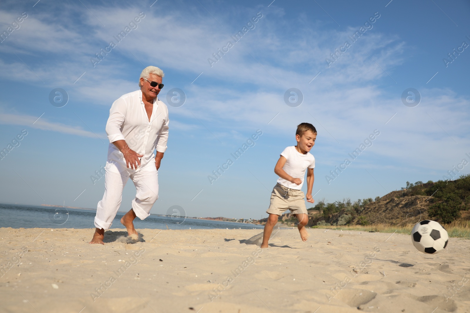 Photo of Cute little boy and grandfather playing with soccer ball on sea beach