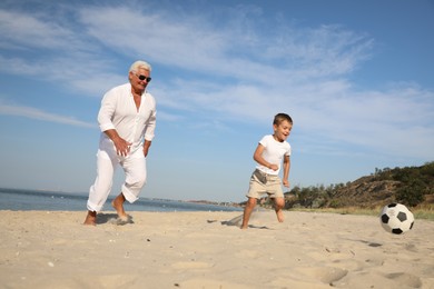 Photo of Cute little boy and grandfather playing with soccer ball on sea beach