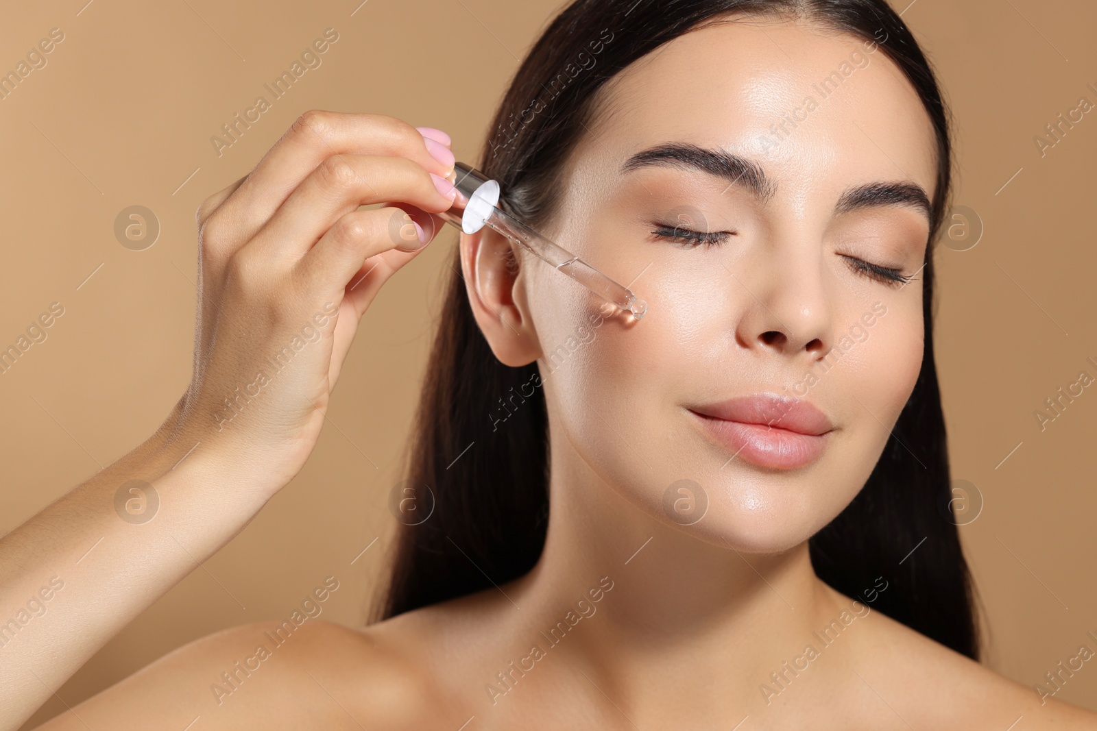 Photo of Beautiful young woman applying serum onto her face on beige background, closeup