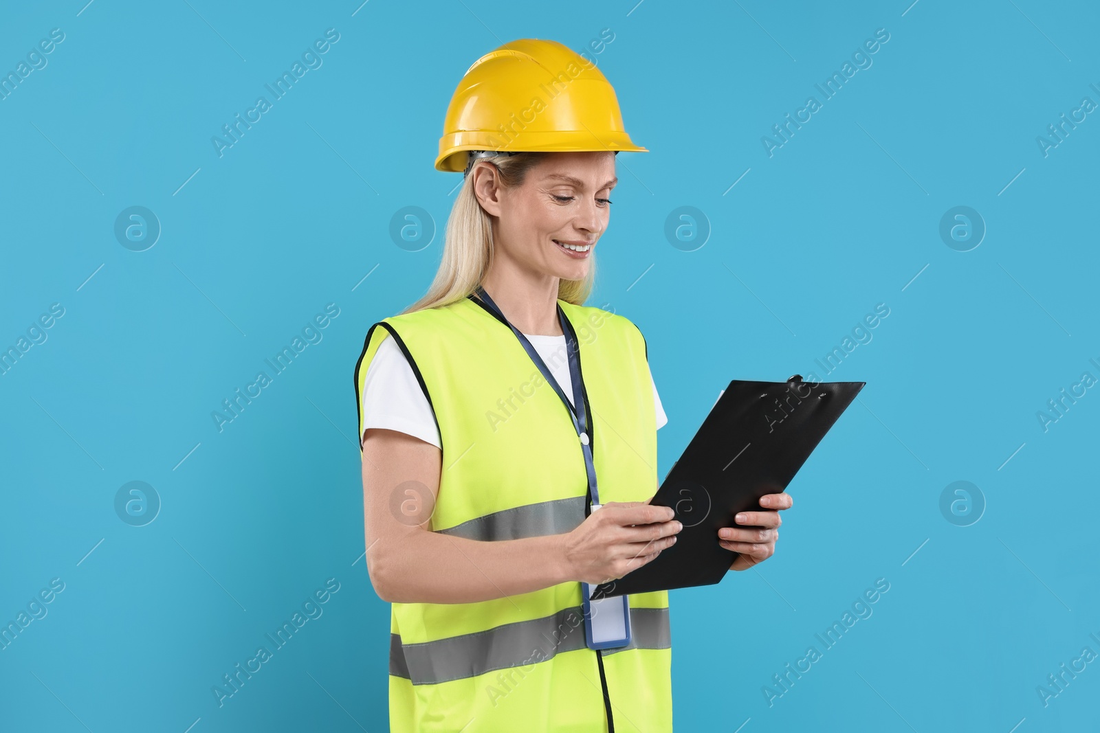 Photo of Engineer in hard hat holding clipboard on light blue background