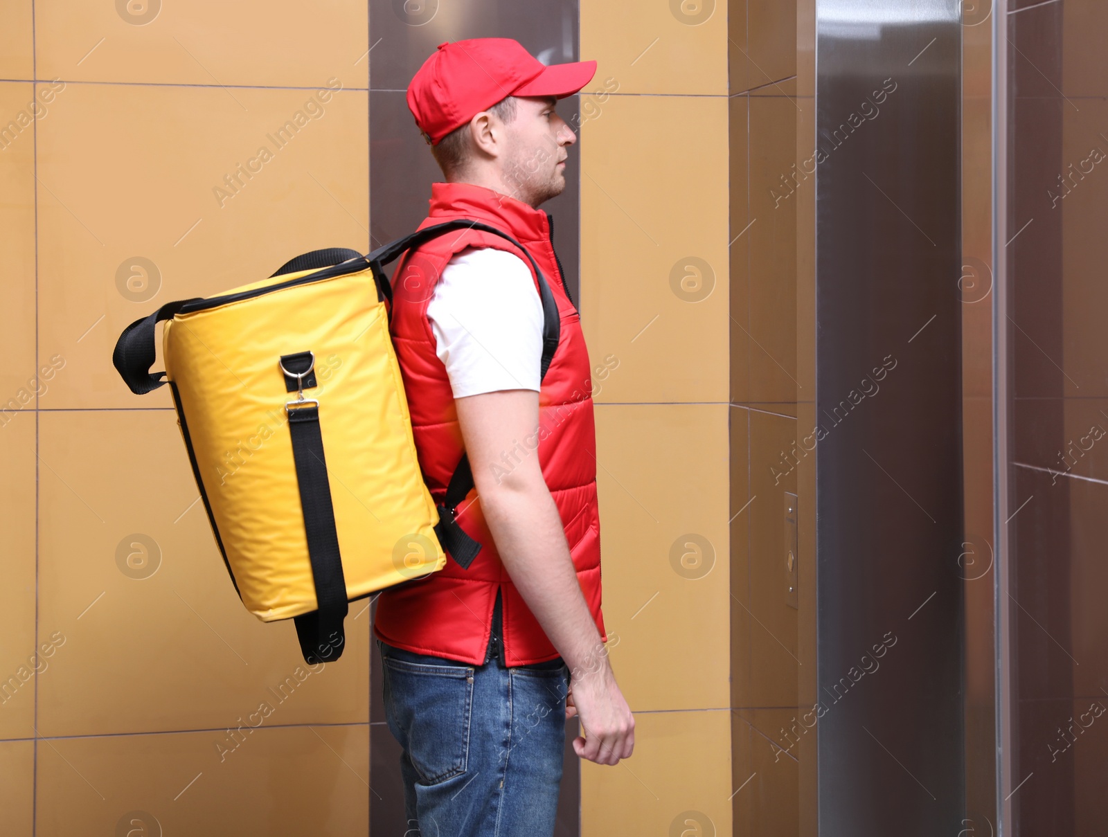 Photo of Male courier with thermo bag waiting for elevator. Food delivery service