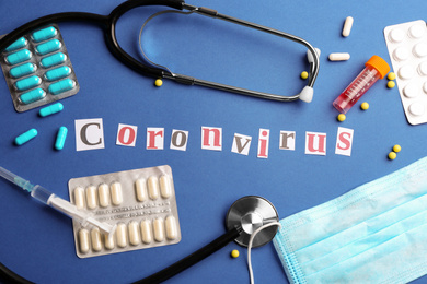 Photo of Flat lay composition with word CORONAVIRUS, stethoscope and medicine on blue background